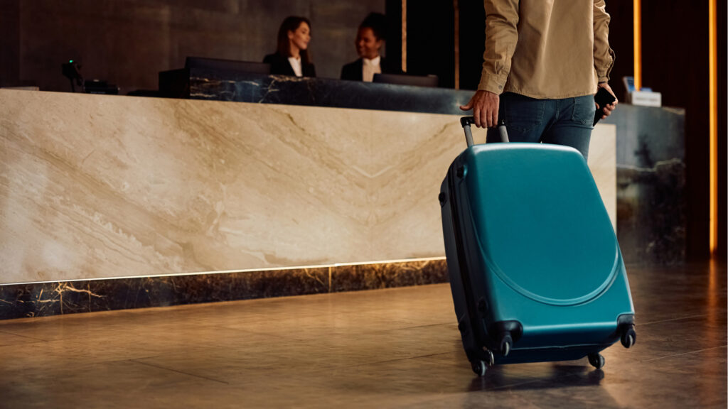 Gast mit Rollkoffer beim Check-in in einem modernen Hotel mit Empfangsbereich und Rezeption im Hintergrund.