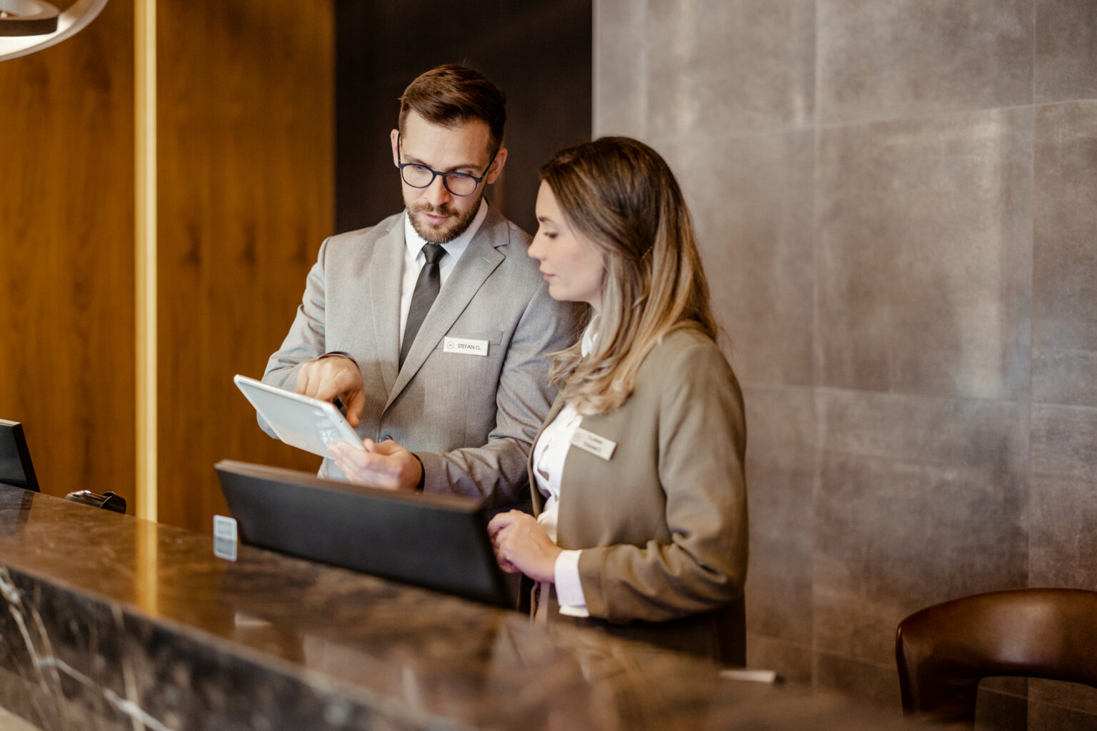 Zwei Mitarbeitende an der Hotelrezeption betrachten gemeinsam ein Tablet und besprechen digitale Prozesse im Hotelbetrieb.